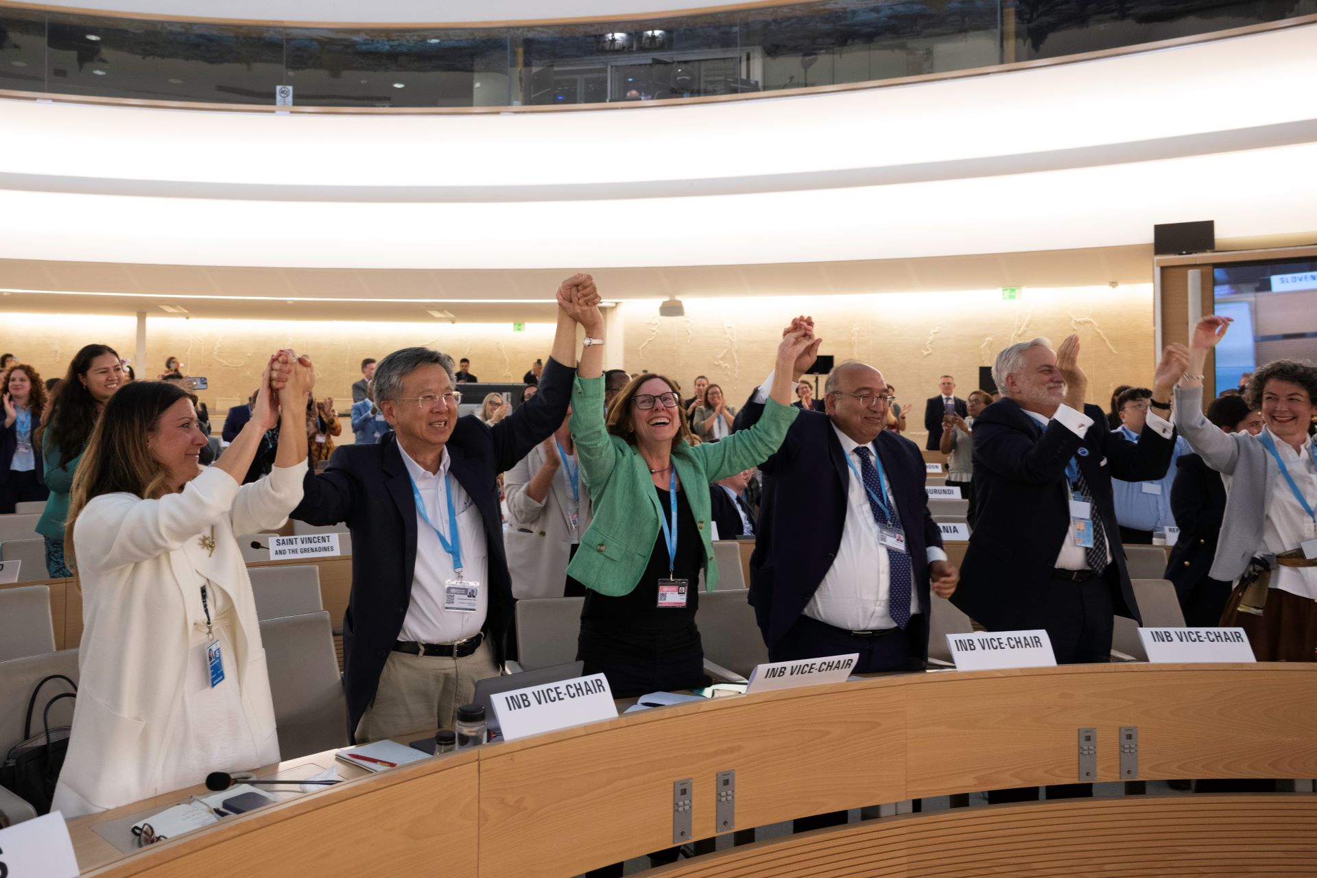 Smiling row or people standing in a conference room with their hands raised and joined.